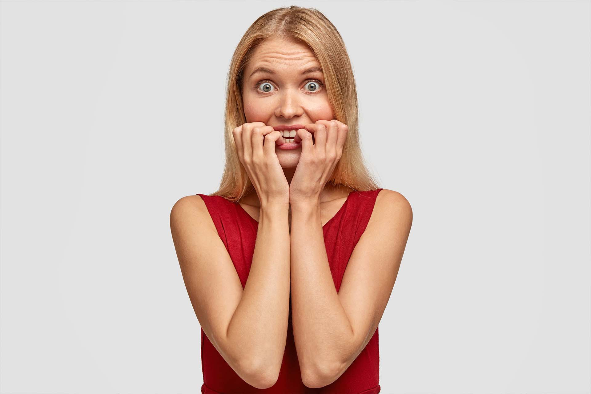 A woman in a red dress biting her fingernails, looking anxious and overwhelmed, embodying the emotional distress of FOMO
